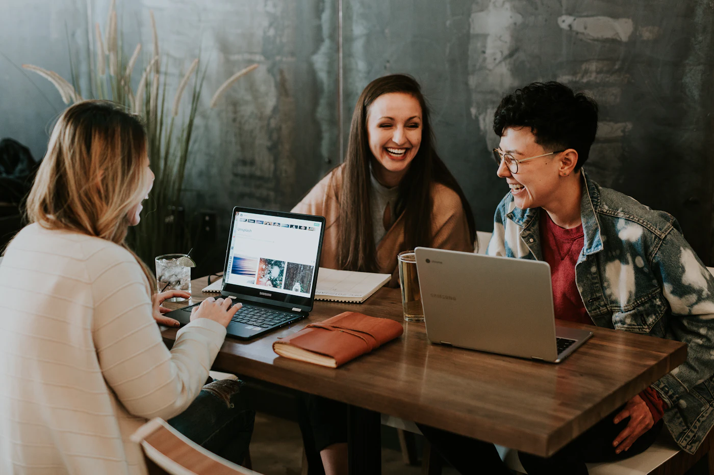 Three colleagues laughing together around a laptop in a bright office